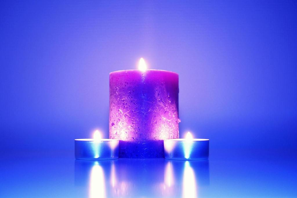 A large maroon candle in the centre is flanked by two tealights to the front, against a purple background.